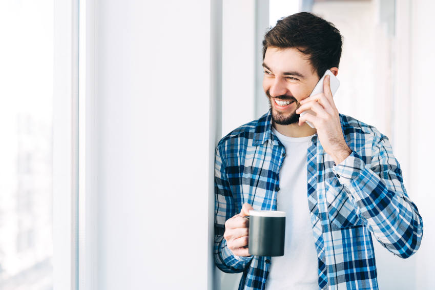 Man with cup of coffee smiling whilst talking on the phone